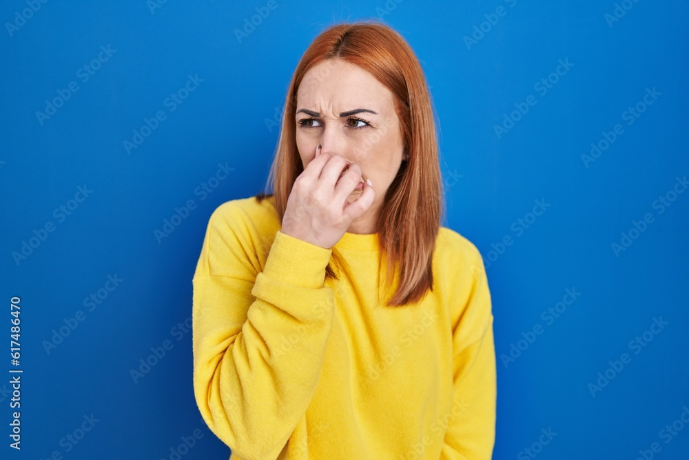 Young woman standing over blue background smelling something stinky and disgusting, intolerable smell, holding breath with fingers on nose. bad smell Young woman standing over blue background smelling something stinky and disgusting, intolerable smell, holding breath with fingers on nose. bad smell