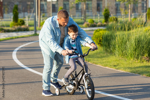 Father teaching son riding bike. Father helping excited son to ride a bicycle in american neighborhood. Child learning to ride cycle with his dad. Fathers day.