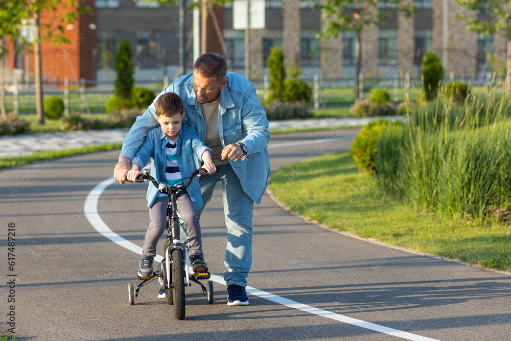 Father teaching son riding bike. Father helping excited son to ride a bicycle in american neighborhood. Child learning to ride cycle with his dad. Fathers day. Father teaching son riding bike. Father helping excited son to ride a bicycle in american neighborhood. Child learning to ride cycle with his dad. Fathers day.
