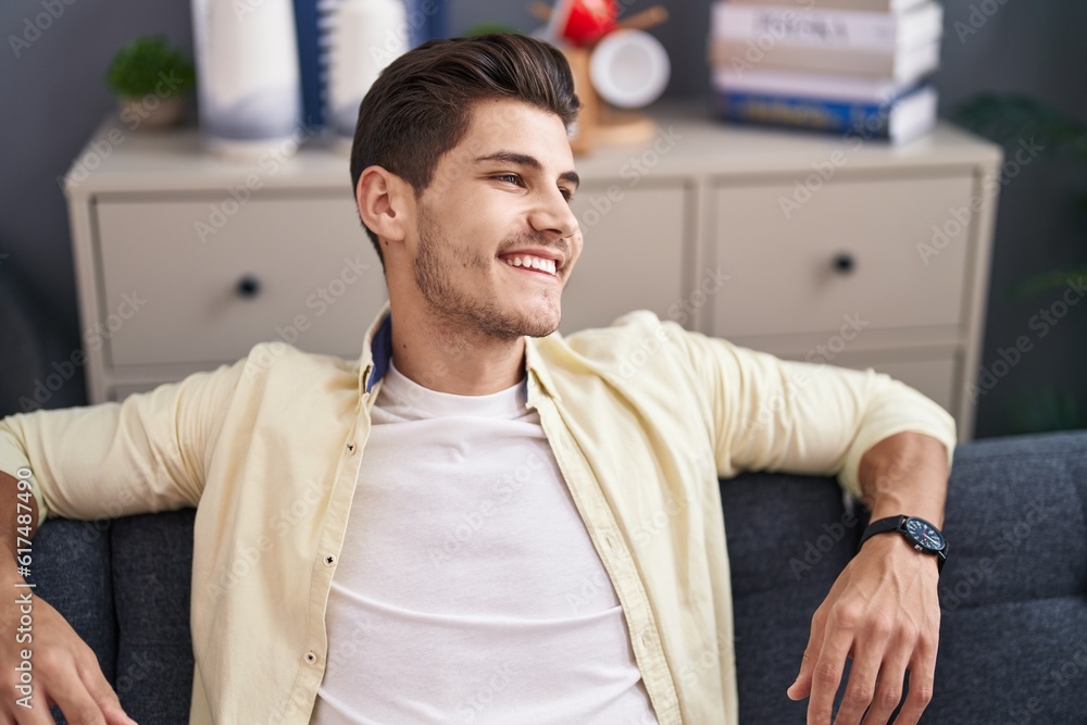 Fototapeta premium Young hispanic man smiling confident sitting on sofa at home