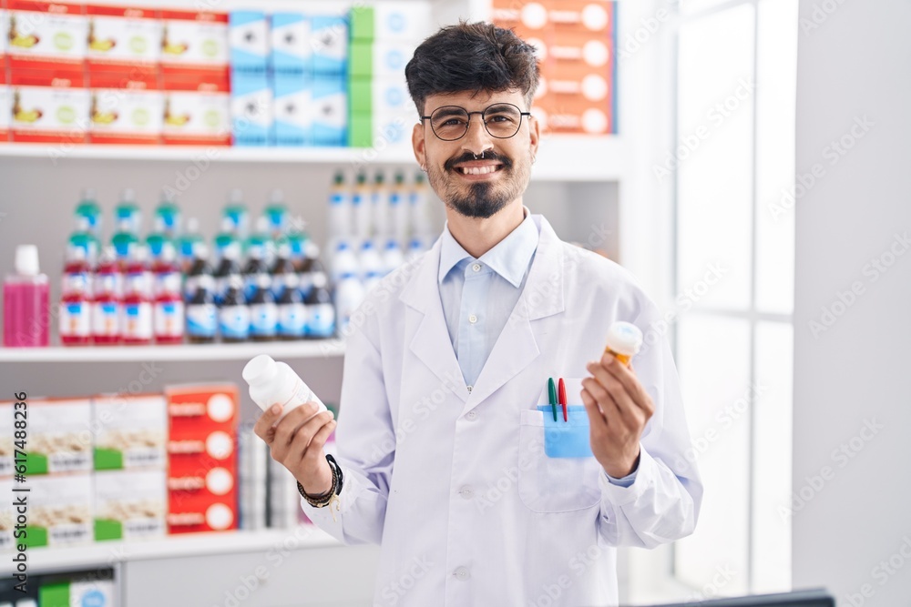 Young hispanic man pharmacist smiling confident holding pills bottles at pharmacy
