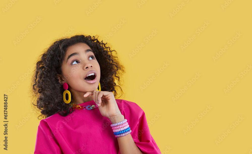 Funny ethnic preteen girl with omg facial expression looks at copy space on yellow background. Stylish dark-skinned curly teen girl with colored accessories delighted looking at promotional product. Funny ethnic preteen girl with omg facial expression looks at copy space on yellow background. Stylish dark-skinned curly teen girl with colored accessories delighted looking at promotional product.