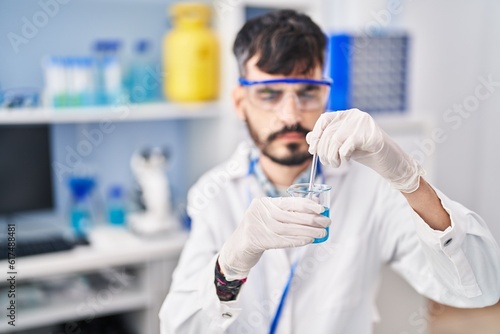 Young hispanic man scientist mixing liquid on glass at laboratory