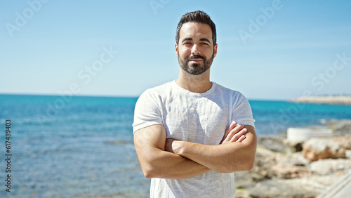 Young hispanic man standing with crossed arms at the beach