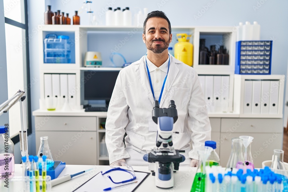 Young hispanic man with beard working at scientist laboratory puffing cheeks with funny face. mouth inflated with air, crazy expression. Young hispanic man with beard working at scientist laboratory puffing cheeks with funny face. mouth inflated with air, crazy expression.