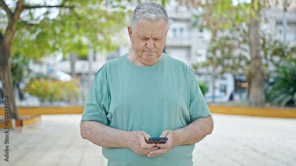 Fototapeta premium Middle age grey-haired man using smartphone with serious expression at park