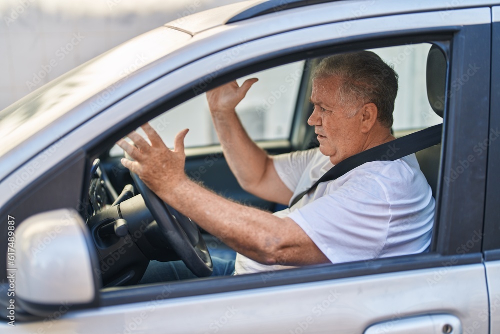 Middle age grey-haired man stressed driving car at street