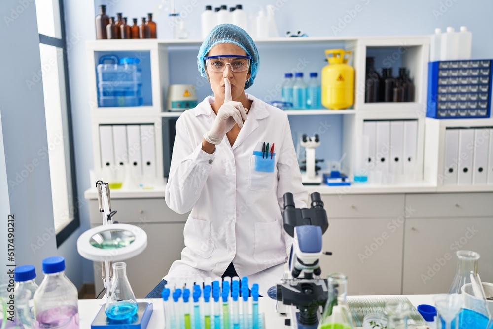 Brunette woman working at scientist laboratory asking to be quiet with finger on lips. silence and secret concept. Brunette woman working at scientist laboratory asking to be quiet with finger on lips. silence and secret concept.