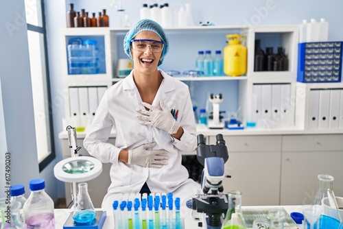 Brunette woman working at scientist laboratory smiling and laughing hard out loud because funny crazy joke with hands on body.