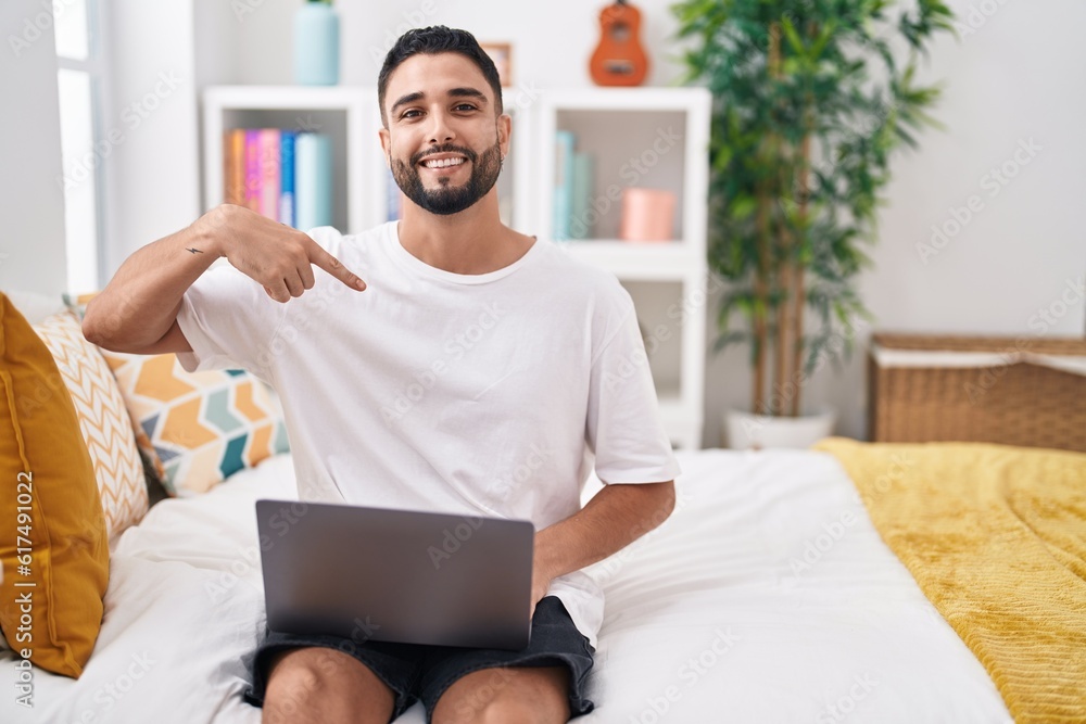 Hispanic young man using computer laptop sitting on the bed pointing finger to one self smiling happy and proud Hispanic young man using computer laptop sitting on the bed pointing finger to one self smiling happy and proud