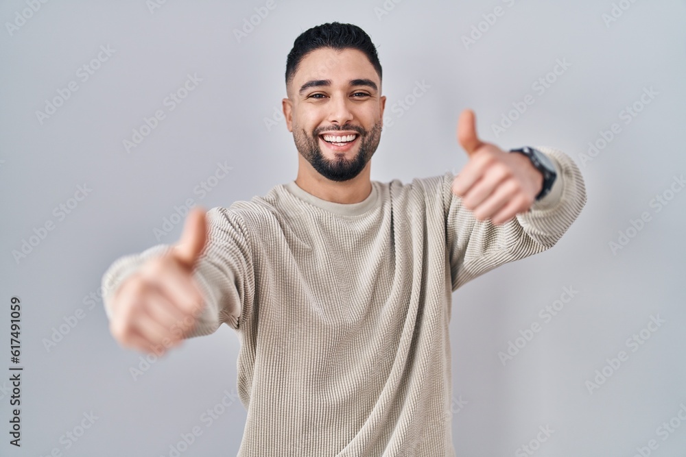 Young handsome man standing over isolated background approving doing positive gesture with hand, thumbs up smiling and happy for success. winner gesture. Young handsome man standing over isolated background approving doing positive gesture with hand, thumbs up smiling and happy for success. winner gesture.