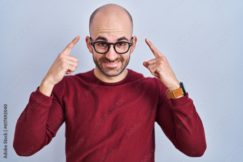 Naklejka premium Young bald man with beard standing over white background wearing glasses smiling pointing to head with both hands finger, great idea or thought, good memory
