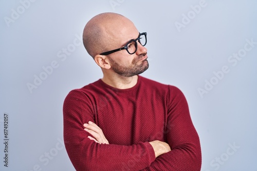 Young bald man with beard standing over white background wearing glasses looking to the side with arms crossed convinced and confident © Krakenimages.com