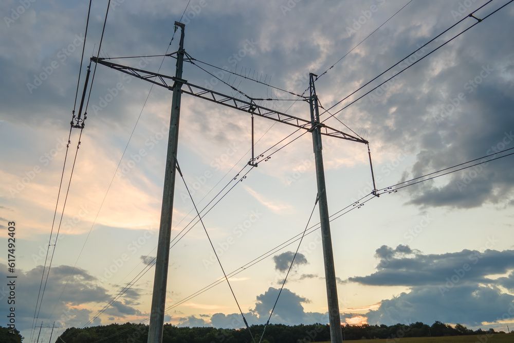 Dark silhouette of high voltage tower with electric power lines at sunrise