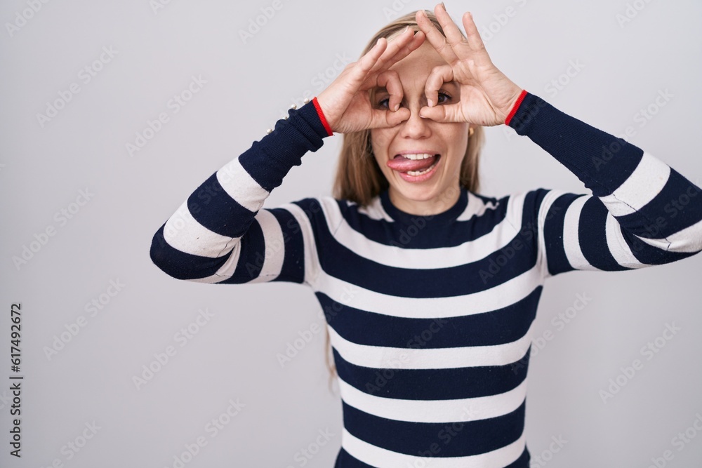 Young caucasian woman wearing casual navy sweater doing ok gesture like binoculars sticking tongue out, eyes looking through fingers. crazy expression. Young caucasian woman wearing casual navy sweater doing ok gesture like binoculars sticking tongue out, eyes looking through fingers. crazy expression.