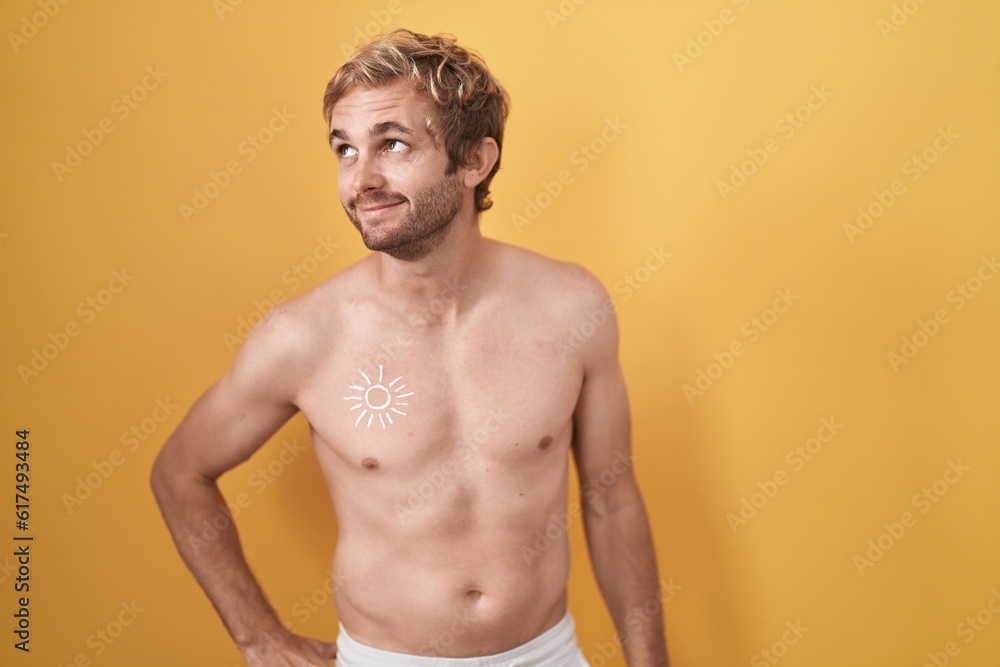 Caucasian man standing shirtless wearing sun screen smiling looking to the side and staring away thinking.