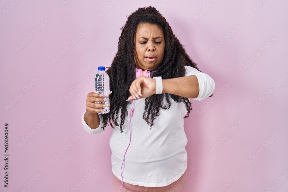 Plus size hispanic woman wearing sportswear and headphones looking at the watch time worried, afraid of getting late Plus size hispanic woman wearing sportswear and headphones looking at the watch time worried, afraid of getting late