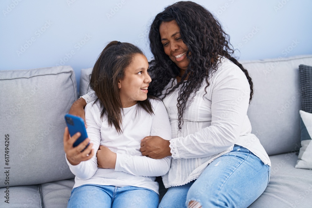 Mother and daughter using smartphone sitting on sofa at home