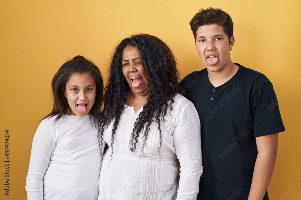 Family of mother, daughter and son standing over yellow background sticking tongue out happy with funny expression. emotion concept. Family of mother, daughter and son standing over yellow background sticking tongue out happy with funny expression. emotion concept.
