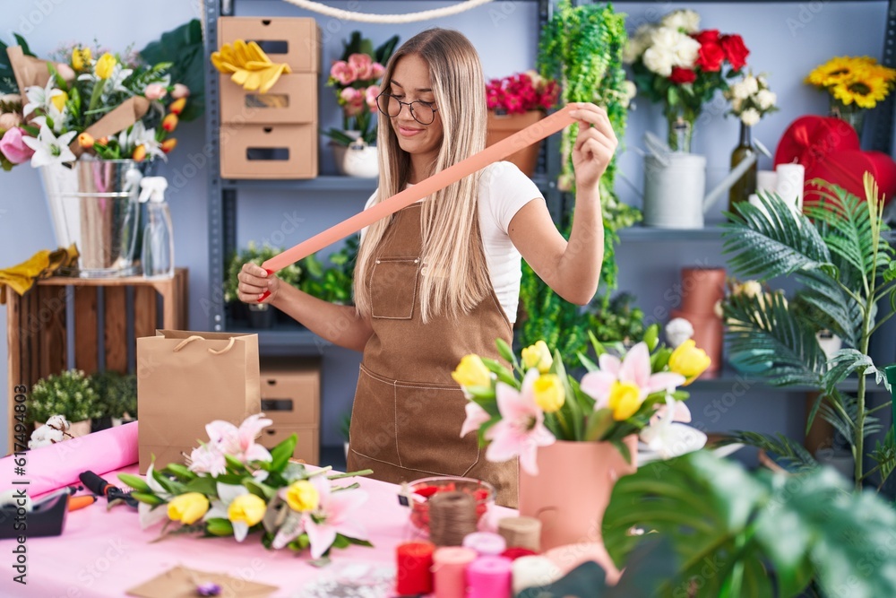 Young beautiful hispanic woman florist make bouquet of flowers holding lace at flower shop