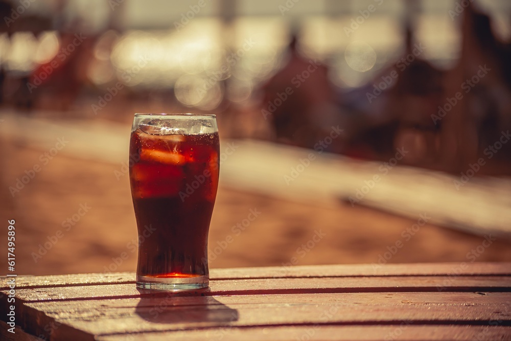 Glass with cola buried in the sand of a beach
