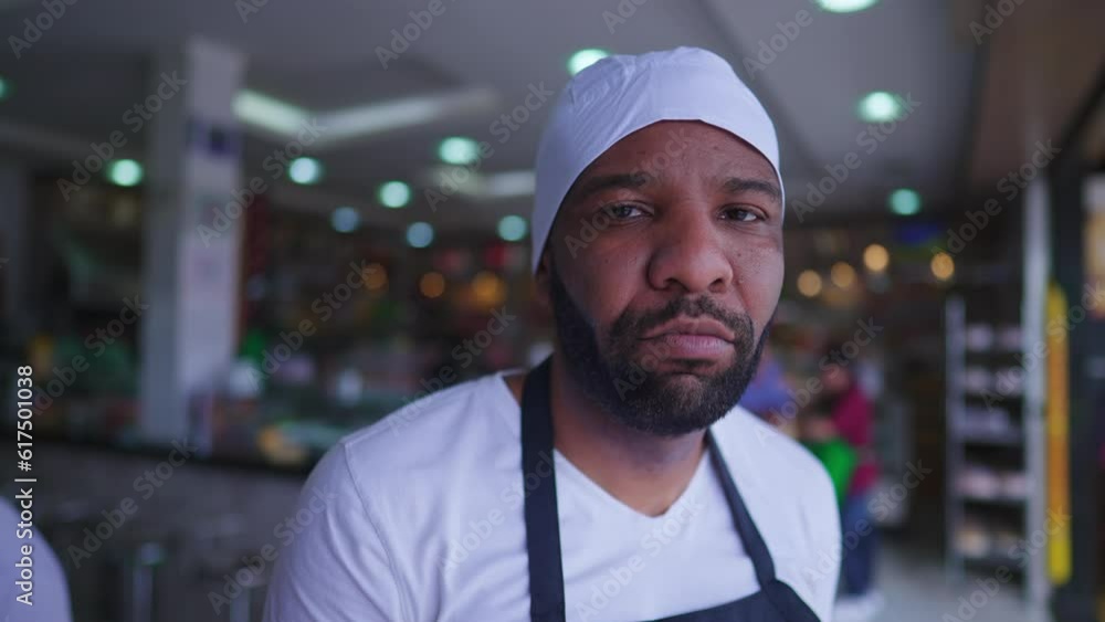One serious black employee standing inside restaurant cafeteria with sad expression, wearing uniform. Young male African American staff One serious black employee standing inside restaurant cafeteria with sad expression, wearing uniform. Young male African American staff
