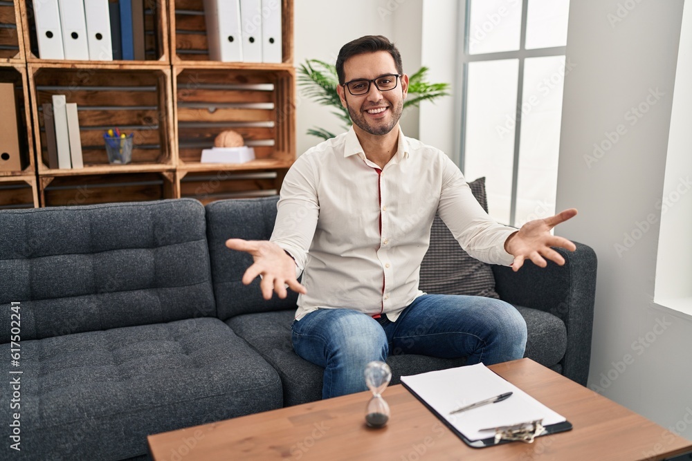 Young hispanic man with beard working at consultation office smiling cheerful offering hands giving assistance and acceptance. Young hispanic man with beard working at consultation office smiling cheerful offering hands giving assistance and acceptance.