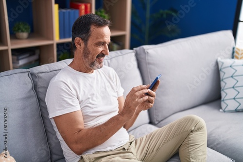 Middle age man using smartphone sitting on sofa at home © Krakenimages.com