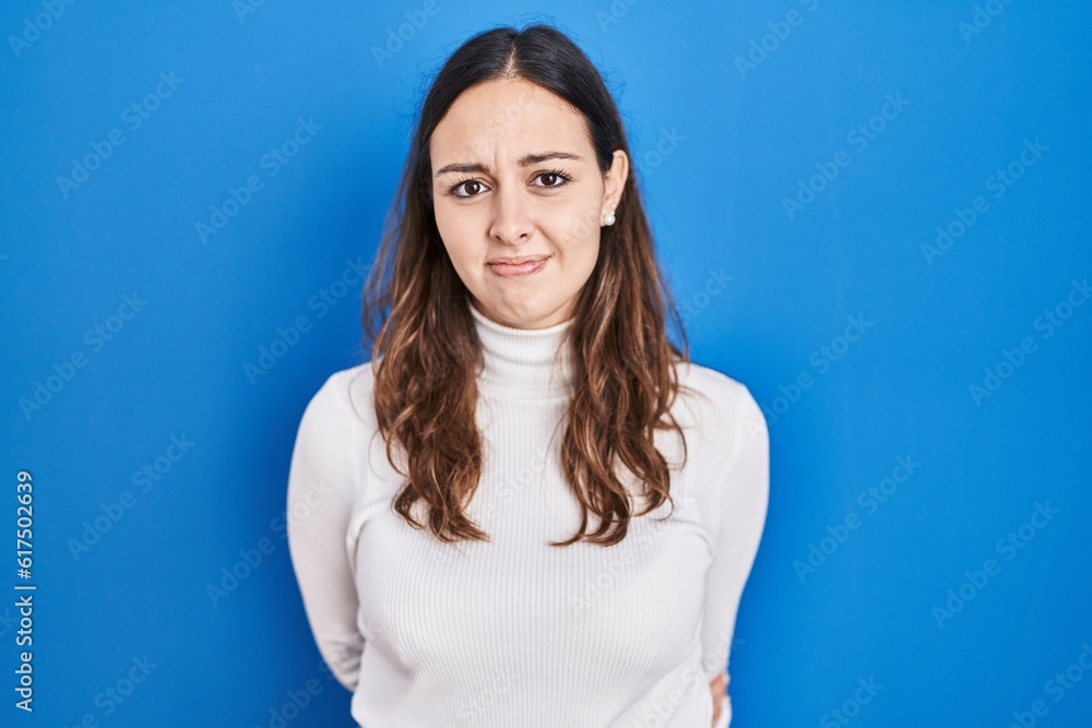 Young hispanic woman standing over blue background skeptic and nervous, frowning upset because of problem. negative person. Young hispanic woman standing over blue background skeptic and nervous, frowning upset because of problem. negative person.