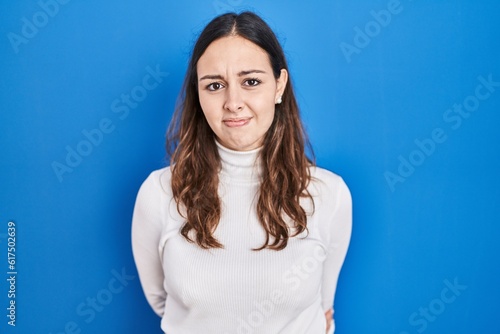 Young hispanic woman standing over blue background skeptic and nervous, frowning upset because of problem. negative person. © Krakenimages.com