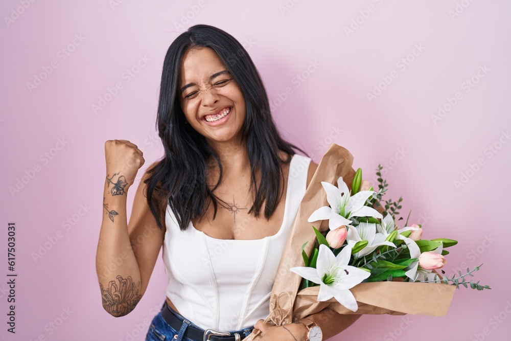 Brunette woman holding bouquet of white flowers very happy and excited doing winner gesture with arms raised, smiling and screaming for success. celebration concept. Brunette woman holding bouquet of white flowers very happy and excited doing winner gesture with arms raised, smiling and screaming for success. celebration concept.