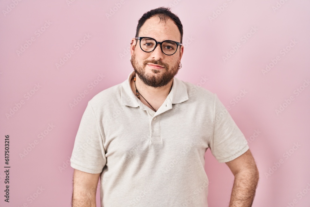 Plus size hispanic man with beard standing over pink background relaxed with serious expression on face. simple and natural looking at the camera. Plus size hispanic man with beard standing over pink background relaxed with serious expression on face. simple and natural looking at the camera.