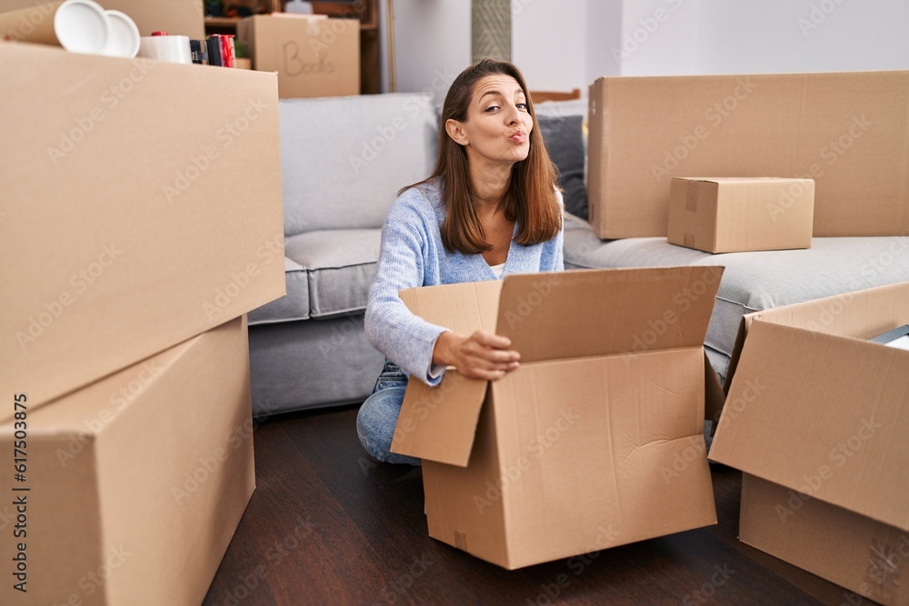 Young woman moving to a new home looking inside cardboard box looking at the camera blowing a kiss being lovely and sexy. love expression. Young woman moving to a new home looking inside cardboard box looking at the camera blowing a kiss being lovely and sexy. love expression.