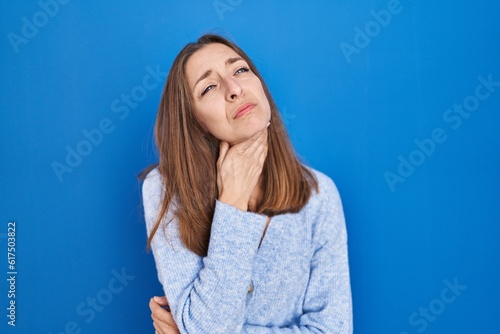 Young woman standing over blue background touching painful neck, sore throat for flu, clod and infection