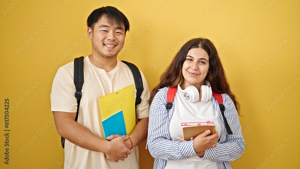 Man and woman students smiling confident holding books over isolated yellow background Man and woman students smiling confident holding books over isolated yellow background