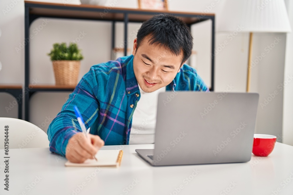 Young chinese man using laptop writing on notebook at home Young chinese man using laptop writing on notebook at home