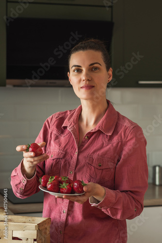 Wallpaper Mural A smiling mature woman holds a strawberry berry next to a basket on the table in a bright kitchen. I cook jam, salad and eat fresh berries. Healthy eco-farm, organic homemade food Torontodigital.ca