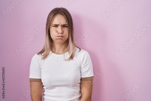 Blonde caucasian woman standing over pink background puffing cheeks with funny face. mouth inflated with air, crazy expression.