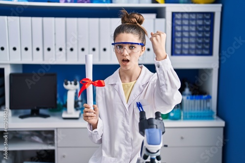 Teenager girl working at scientist laboratory holding degree annoyed and frustrated shouting with anger  yelling crazy with anger and hand raised