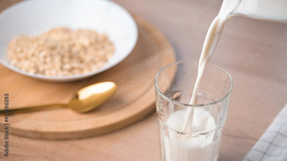 Pouring milk in a glass on wooden kitchen table. Glass with kefir or milk on the table. Drinking fresh lactose-free milk. Healthy breakfast with milk and cereal oatmeal. Pouring milk in a glass on wooden kitchen table. Glass with kefir or milk on the table. Drinking fresh lactose-free milk. Healthy breakfast with milk and cereal oatmeal.