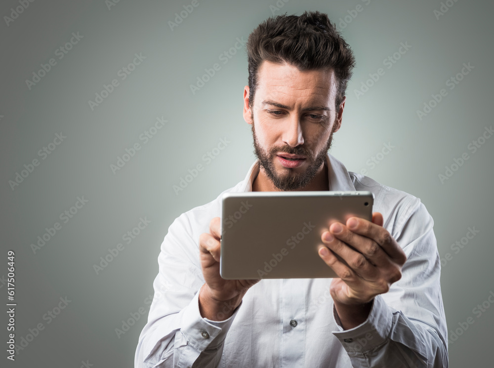 Attractive young man using a digital tablet on gray background Attractive young man using a digital tablet on gray background