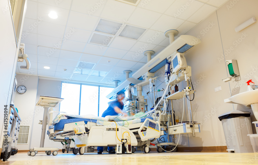 A hospital room with modern medical equipment and blurred patient and nurse or doctor figures. A hospital room with modern medical equipment and blurred patient and nurse or doctor figures.
