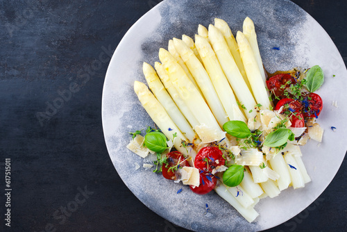 White asparagus glazed with cherry tomatoes and parmesan cheese served as top view on a design plate with text space left