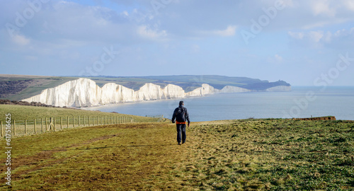 Rear view of a solo male hiker walking towards Seven Sister cliff in England in a sunny day