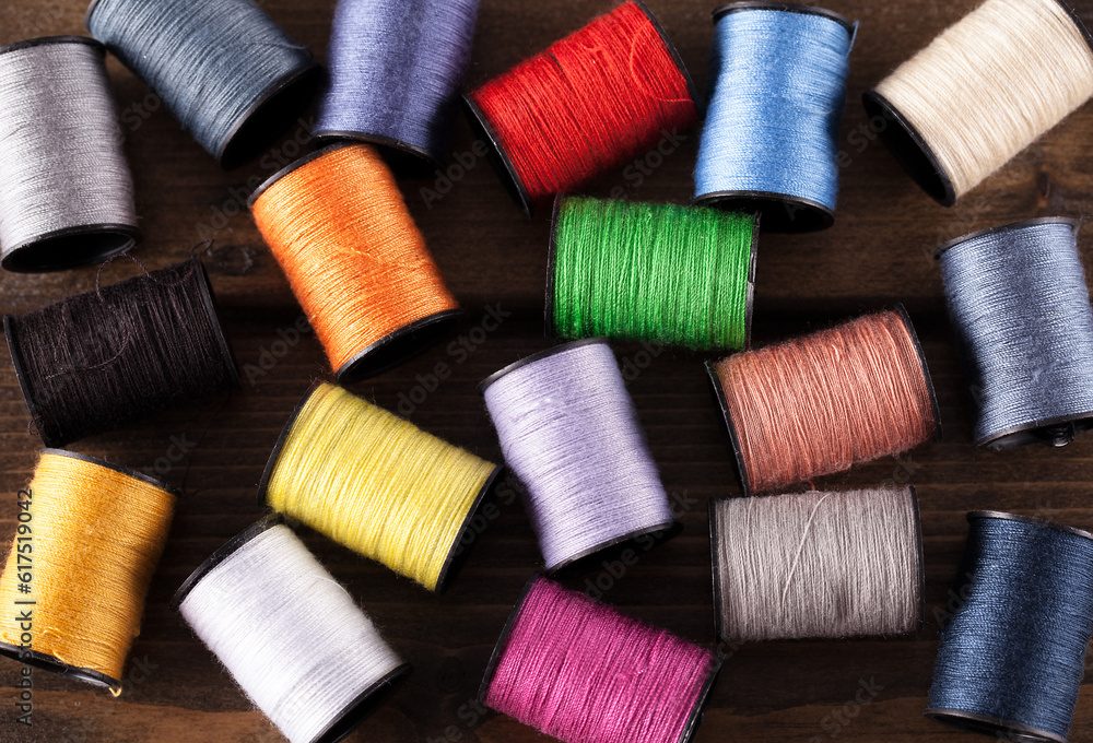 Colorful cotton reels scattered across a dark rustic wooden table Colorful cotton reels scattered across a dark rustic wooden table