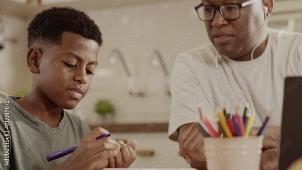 homem Brasileiro trabalhando no computador portatil na mesa cozinha de sua casa no Brasil enquanto ajuda seu filho com o trabalho escolar homem Brasileiro trabalhando no computador portatil na mesa cozinha de sua casa no Brasil enquanto ajuda seu filho com o trabalho escolar