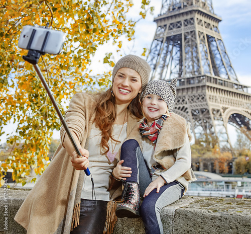 Autumn getaways in Paris with family. happy mother and child tourists on embankment near Eiffel tower in Paris, France taking selfie using selfie stick © Designpics