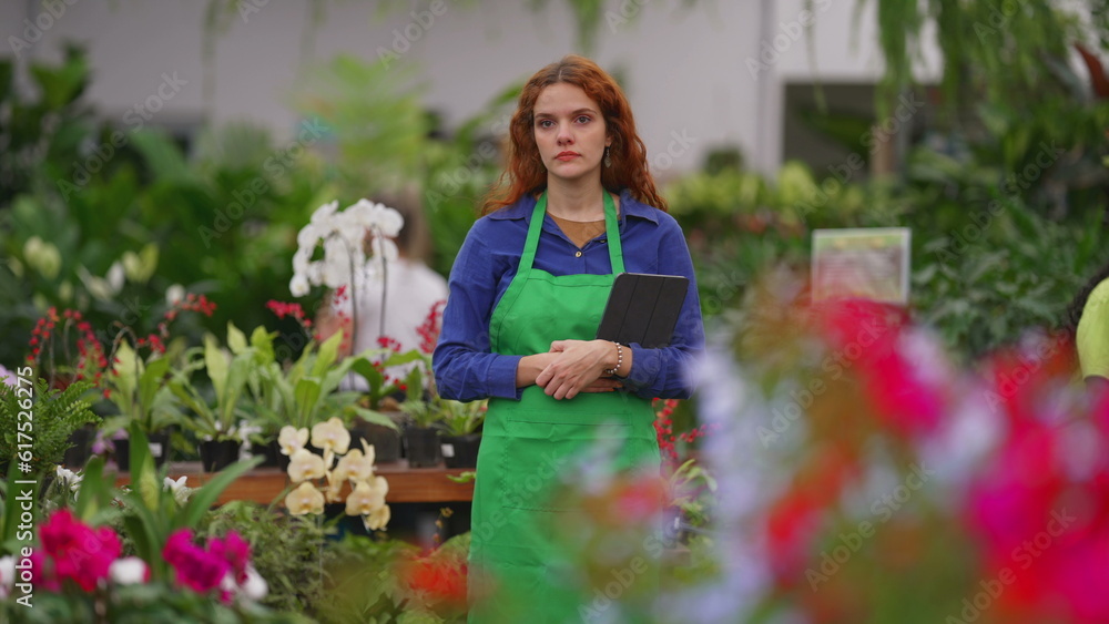 Candid pensive female Florist employee standing inside flower shop. Contemplative woman daydreaming at plant retail store