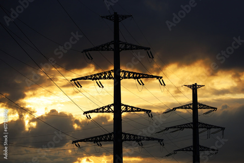 Silhouettes of high voltage tower with electrical wires on background of sunset sky and dark clouds. Electricity transmission lines, power supply, blackout concept