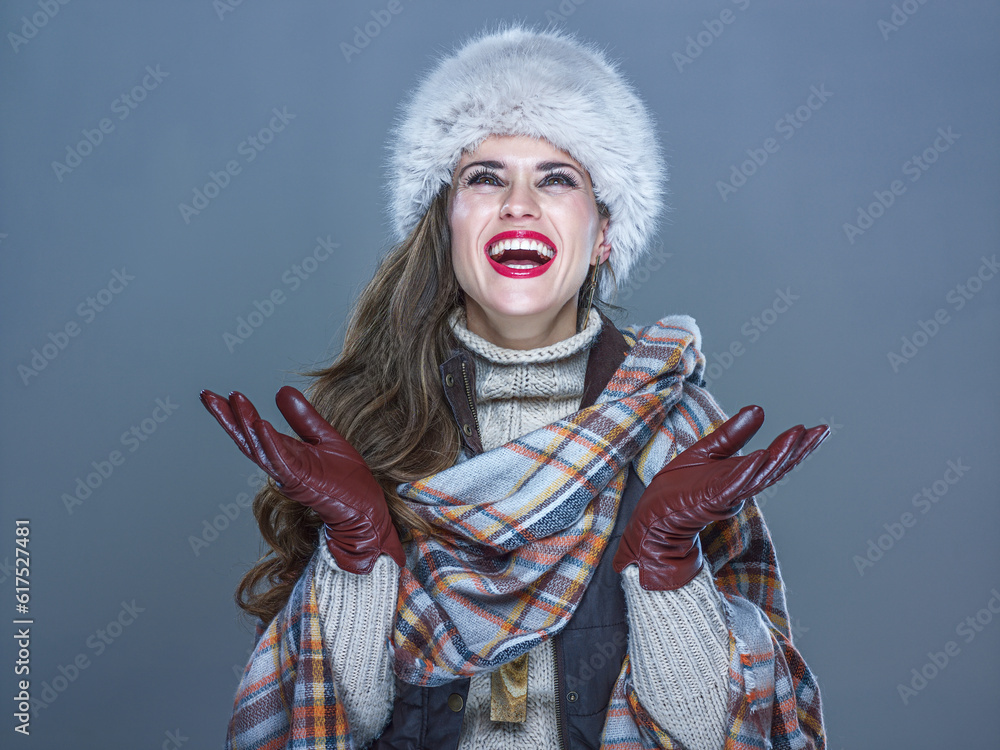 Winter things. Portrait of smiling trendy woman in fur hat isolated on cold blue catching snowflakes